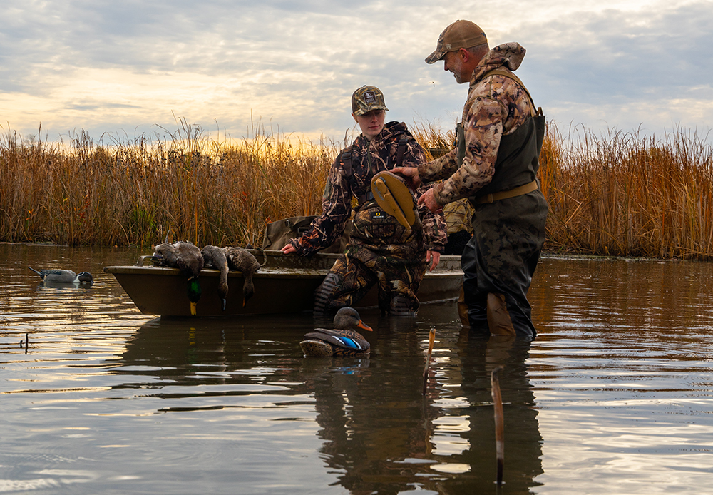 A young hunter gains instruction from an experienced hunter in a body surrounded by long grass. Delta Waterfowl’s HunteR3 and Duck Production Programs received funding from Wildlife Habitat Canada.