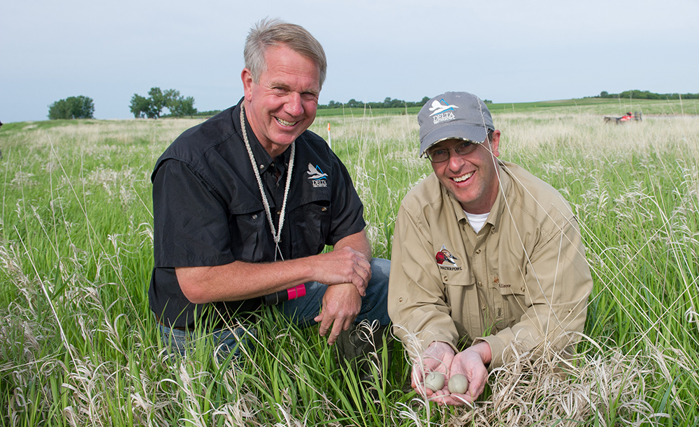 Delta Waterfowl staff are pictured happy in a field, holding a pair of duck eggs.